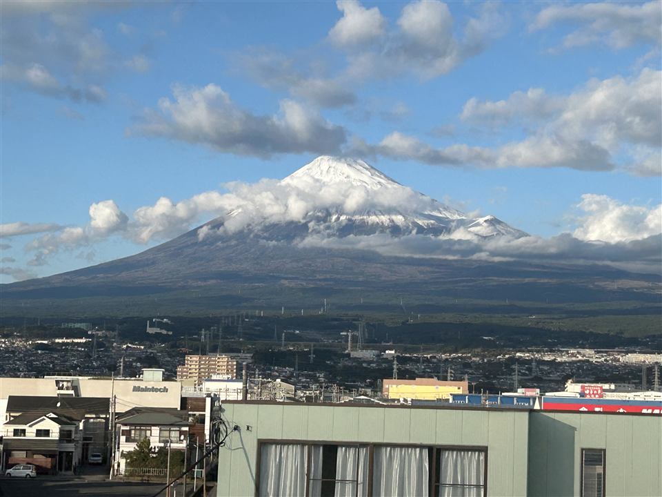 Snow-capped Mt. Fuji under clouds, seen over the rooftops of Fuji City